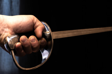 Old sword or dagger in man's hand on black background.