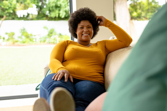 Full length portrait of smiling african american mid adult woman sitting on couch at home