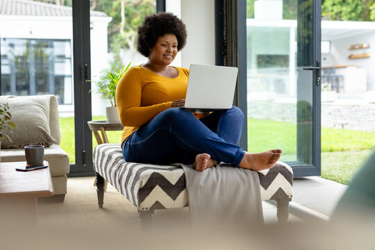 Smiling african american mid adult woman using laptop while sitting on couch at home
