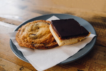Sweet baked goods like bars and cookies on plate on wooden background.
