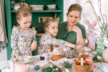 easter holiday time in spring season. happy family candid little kids sisters girls together mother have fun at home decorating table for lunch or dinner. traditional food. festive home decor