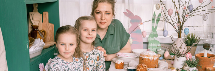 easter. happy family mom together little kids girls have fun springtime Easter holiday at home setting and decorating table scape with Easter cakes bakery and painted eggs for lunch or dinner. banner