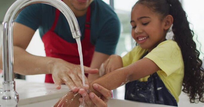 Happy biracial father and daughter washing hands in kitchen