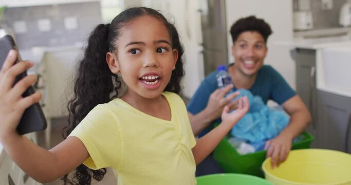 Happy biracial father and daughter making video call using smartphone, sorting waste together