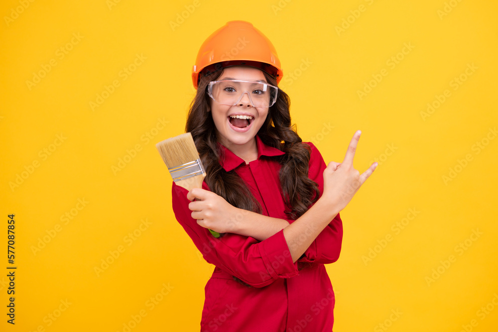 Canvas Prints Child builder in helmet. Teenage girl painter with painting brush tool or paint roller. Child on repairing work isolated on yellow background. Kids renovation concept. Happy teenager girl.