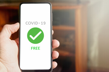 Male hand holding mobile phone with text "Covid-19 Free" on the screen. Person checking health report of covid test on mobile app at home. Copy space.