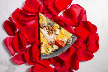 Top view of black dough pizza slice on marble background with rose petals. Romantic scene with food. Pizza with chicken, blue cheese, mushrooms and cherry tomatoes