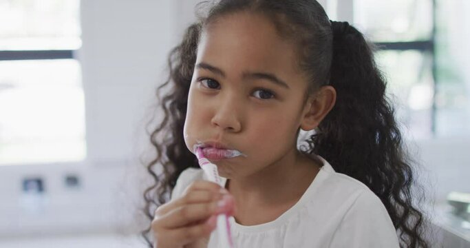 Portrait of happy biracial girl looking at camera and brushing teeth