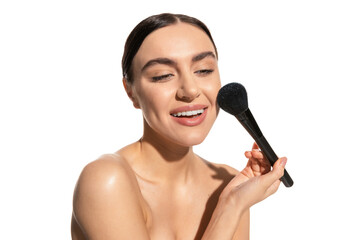 cheerful young woman with bare shoulders holding soft powder brush near cheek isolated on white.