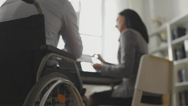 Closeup of man wheelchair user sharing ideas with female colleague in office