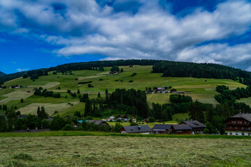 Obraz premium Rural mountain landscape in Italy in the Dolomites. Amazing bright colorful spring and summer landscape. Green blooming fields, wooded mountains and blue sky with clouds. Natural landscape, Europe.