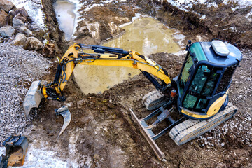 A small yellow excavator on a construction site. Laying of foundations and drainage.