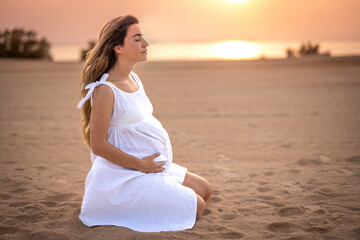 Fototapeta na wymiar Thoughtful and relaxed pregnant woman sitting on sand and meditating on the beach at sunset.