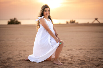 Fototapeta na wymiar Beautiful young pregnant woman in white dress posing on the beach at sunset.