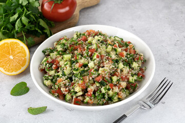 Levantine vegetarian Tabouleh salad with quinoa, tomatoes, cucumbers, parsley, lemon on white background.