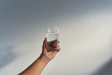 Vaso con agua sobre una pared blanca y luz del sol   