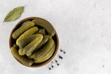 Pickled cucumbers in a wooden bowl with spices on gray background. Marinated pickled cucumbers. Top...