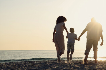 Fototapeta premium Silhouette, beach and a family with kids by the ocean, holding hands in nature at sunset from the back. Summer, travel or mockup with a mother, father and child having fun while bonding at the sea