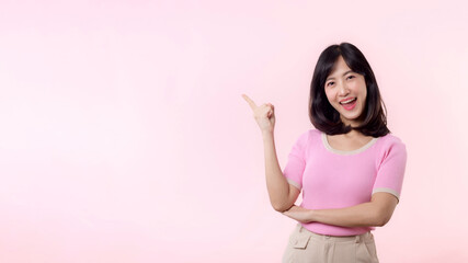 Portrait young beautiful asian woman happy smile pointing finger and hand to showing on copy space isolated on pink background. Attractive female person gesture attention to this promotion.
