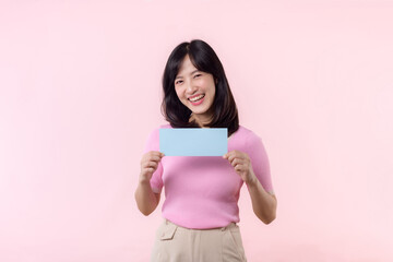 Fototapeta premium Portrait happy young woman model holding and showing blank space paper for advertisement information message poster with thumb up or point finger gesture isolated on pink pastel studio background.