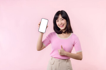 Portrait beautiful young asian woman happy smile showing smartphone screen with pointing finger hand gesture to mobile phone isolated on pink pastel studio background. Blank screen smartphone concept