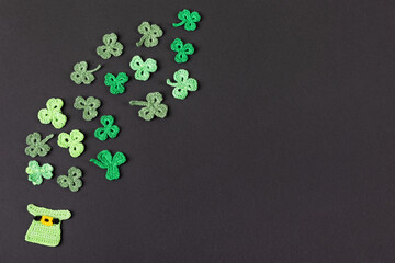 St Patrick's Day concept. Composition made of knitted green shamrocks and hat on a black background. Holiday sign and knitted clover leaf. Copy space, flat lay, place for text