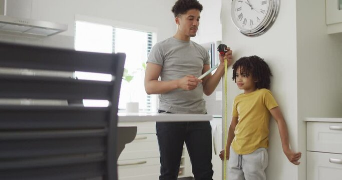 Happy biracial man and his son measure height in kitchen