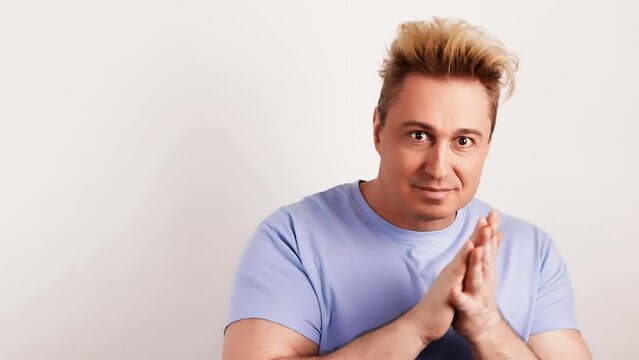 Man rubbing his hands thinking over choice, imagining plan in mind. Positive smiling handsome guy pondering idea, wears blue t-shirt. Indoor studio shot isolated on white background.