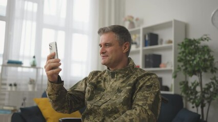 Positive soldier wheelchair user having video call on smartphone with relatives