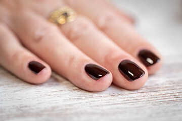 White woman's hand with nails freshly painted dark red on a wooden table.