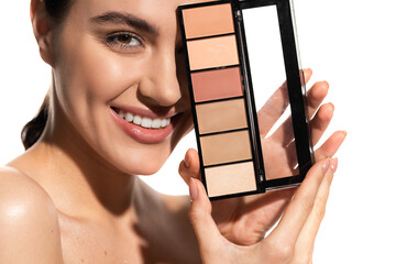 smiling young woman covering eye with eye shadow palette isolated on white.