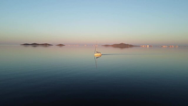 A boat crosses the Mar Menor at sunset. The sea is like a mirror and reflects the image of the boat, the blue sky and the islands. Sense of tranquility, peace and harmony. La Manga, Murcia, Spain