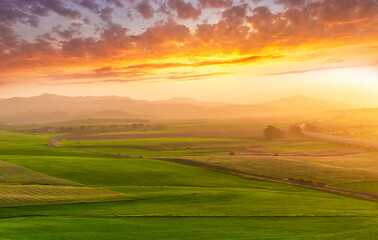 beautiful green valley with green fields with green spring grass with nive hills and mountains and scrnic colorful cloudy sunset on background of landscape
