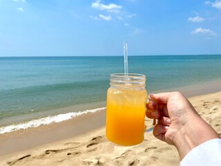 juicy orange juice in a glass with a straw, against the background of the sea and sand