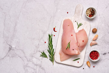 Fresh chicken breast fillet on cutting board with spices and herbs on gray marble background. Preparation for cooking.