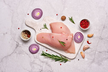 Fresh chicken breast fillet on cutting board with spices and herbs on gray marble background....
