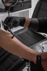 The master shaves the client's hand before applying the tattoo. Black medical gloves. Tattoo salon. 