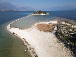 Italy, Lake Garda ,San Biagio Island , Rabbit Island - the shallow waters of the lake allow you to walk and reach the island on foot - water emergency in Lombardy , drought lowering of the water level - obrazy, fototapety, plakaty