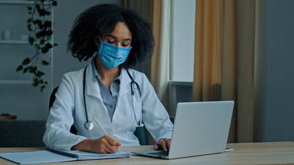 Ethnic african woman doctor therapist cardiologist psychotherapist in medical mask write prescription diagnosis speaking in video chat calling patient distant online treatment during covid-19 epidemic