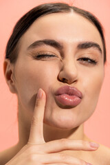 Obraz premium close up of young and brunette woman pouting lips isolated on pink.