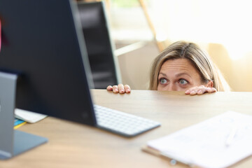 Surprised and excited female peeping out desk and looking at pc screen