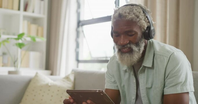Video of african american senior man using tablet and headphones