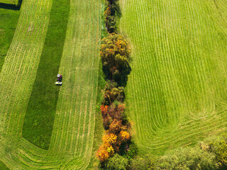 Aerial view of freshly mowed green gras field and a tractor finishing mowing a field