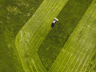 Drone photo of tractor mowing a green grass field in the countryside on a sunny day