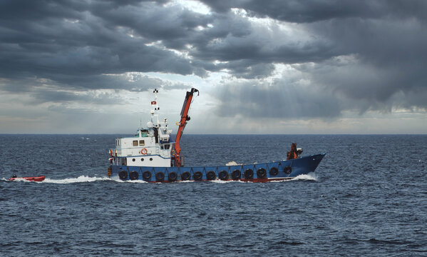A longliner fishing boat in the open sea against a dramatic overcast sky above the horizon