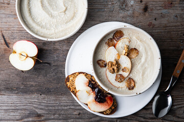 Two bowls of homemade Jerusalem artichoke and apple cream soup and open sandwich with homemade pate with fresh apple and cherry jam on wooden table.