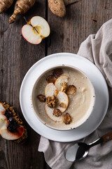 Bowl of homemade Jerusalem artichoke and apple cream soup and toast with homemade pate with fresh apple and cherry jam and fresh sun choke tubers and apple on wooden table.