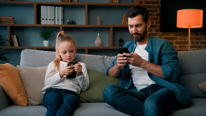 Caucasian single daddy and child kid preschooler girl sit on sofa look at mobile phone screen chatting online use home wifi smartphone apps young family internet addicted modern gadgets tech overuse