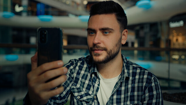 Smiling arabian caucasian male blogger businessman look at mobile phone camera talk video call in shopping mall happy young man chatting online recording blog use modern tech for remote communication