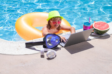 Child relaxing in the pool with laptop. Kid online working on laptop, swimming in a sunny turquoise...